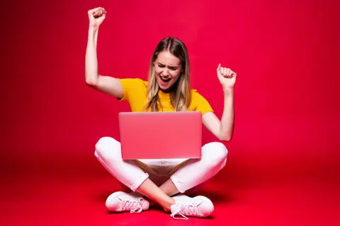 mujer-joven-feliz-gesto-ganador-sentado-suelo-piernas-cruzadas-usando-computadora-portatil-pared-roja.jpg
